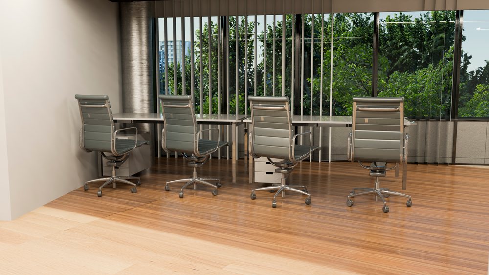 Four modern metal-framed office chairs with wheels aligned beside desks in a contemporary office.