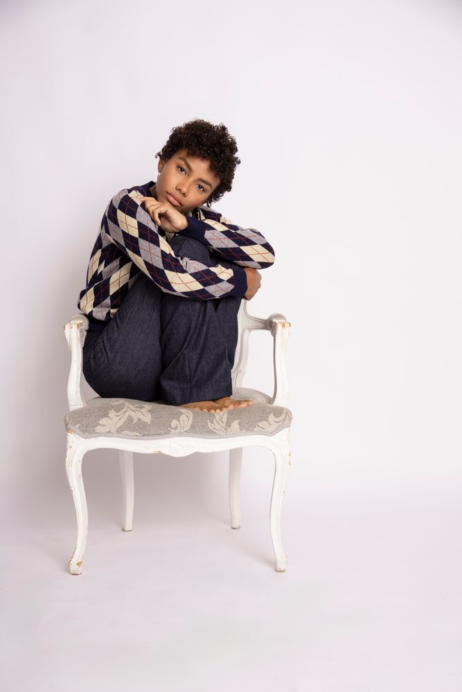 Young woman sitting curled up on an armchair in a studio fashion shoot with a white background.