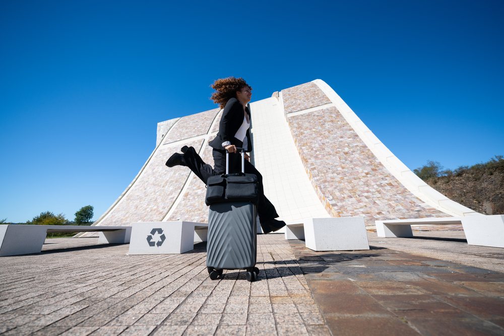Businesswoman jumping with a suitcase outdoors near modern architecture and benches in Santiago de Compostela, traveling executive, Spain, Antiago De Compostela.