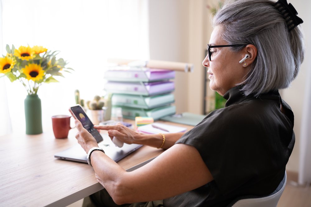 Older woman using smartphone at a bright indoor desk, Spain.