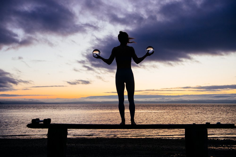 Silhouette of person standing on a bench holding two glass balls at sunset by the ocean beach, WA, USA.