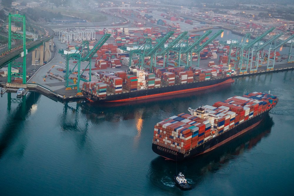 Two container ships loaded with cargo containers at a port terminal with shipping cranes and a tugboat at the, Port of Long Beach, CA, USA.