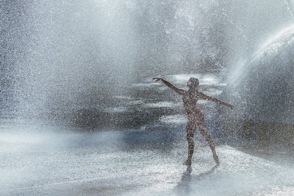 Dancer striking a graceful ballet pose within a fine mist of water droplets in an outdoor setting, partner, acrobatics, yoga, USA.