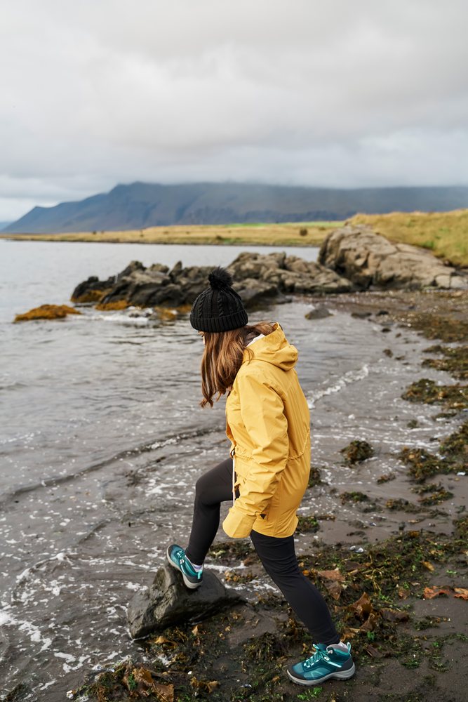 A white woman hikes on a rocky shore by the sea