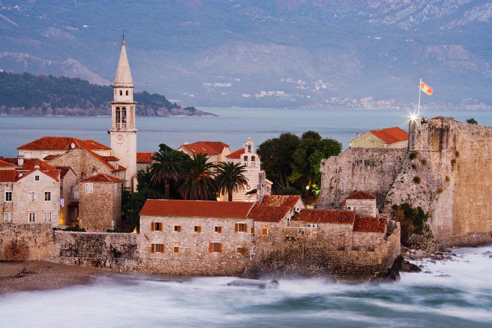 Budva old town and fortress with red tile roofs and stone buildings on Montenegro's Adriatic coast at sunset.