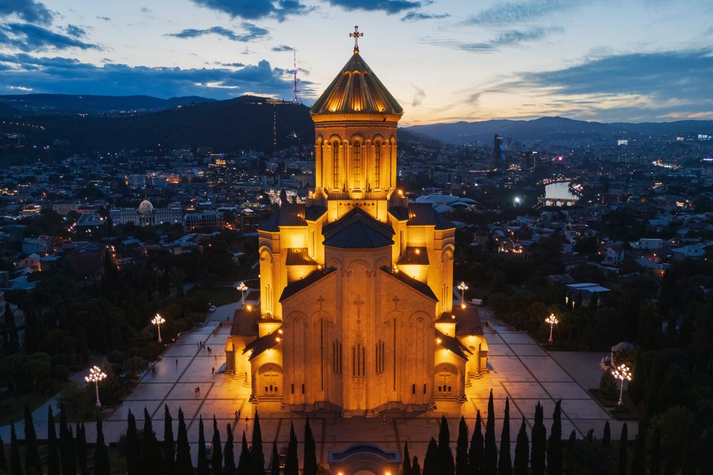 Holy Trinity Cathedral in Tbilisi illuminated at Dusk with city skyline, river, and mountains in the background, Skylines, Georgia.