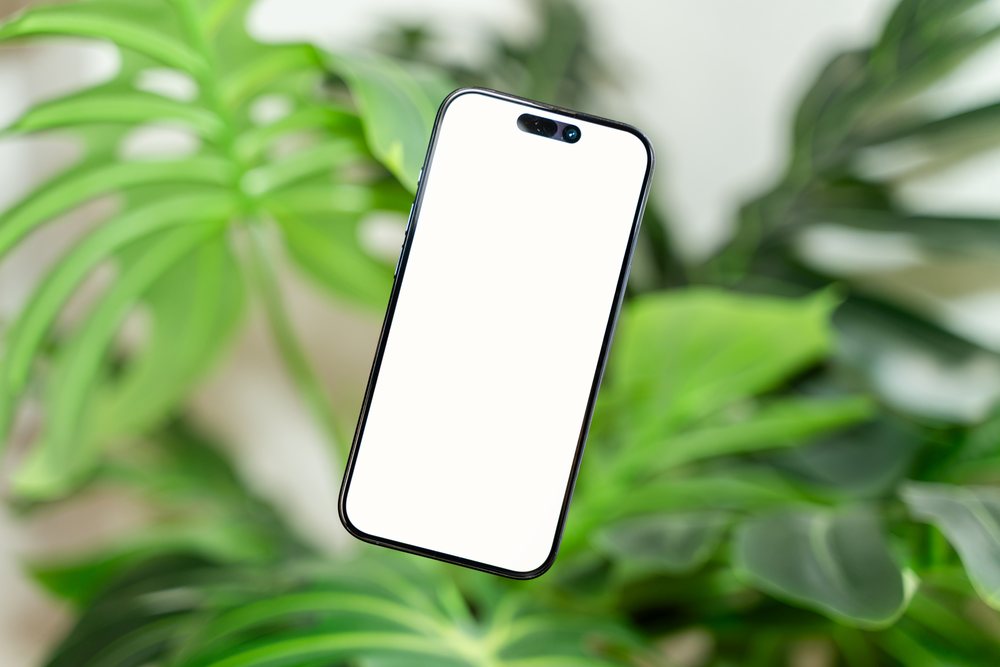 Smartphone with black frame and blank white screen floating before green leafy plants indoors, mock up, Spain.