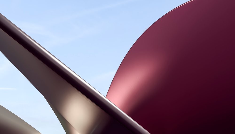 Curved metal sculpture with red and beige surfaces set against a clear blue sky.