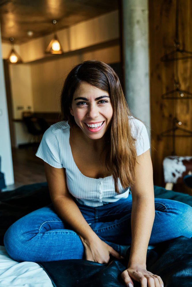 A young woman sitting on a bed smiling in a cozy hotel room in a hotel