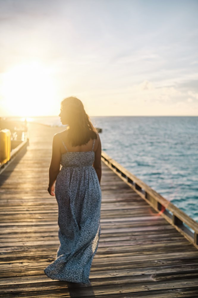 A woman in a long summer dress walks along a wooden pier at sunset by the sea in the, Maldives.