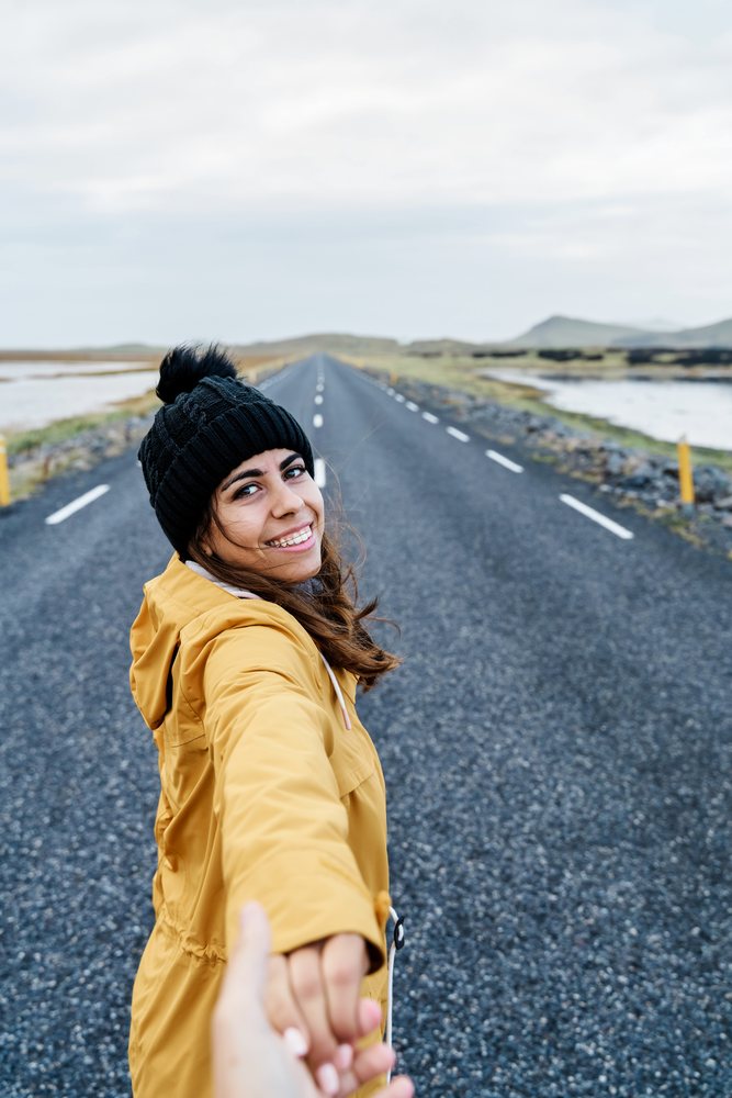 White Woman in warm clothing holding hands and smiling on an open road