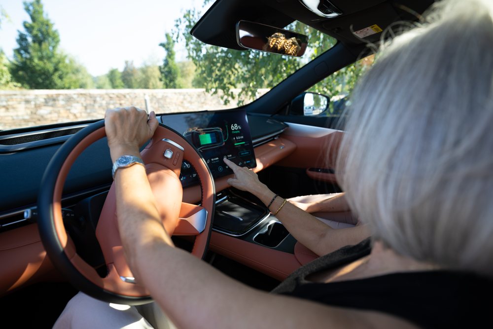 Woman drives an electric car using the touchscreen dashboard on a sunny day with green trees outside, businesswomen, Spain.