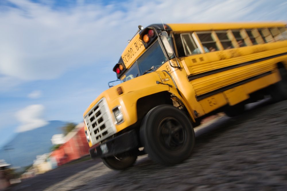 Yellow school bus in motion on a cobblestone street during daytime, Sacatepequez Department, Guatemala.