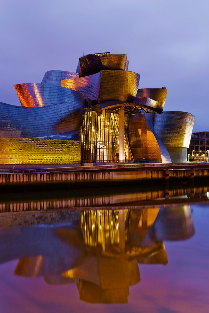 The Guggenheim Museum, Spain is illuminated in the evening, reflecting on the water, Bilbao.