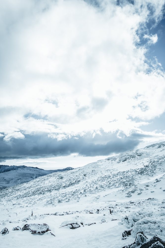 Snow covers a rocky mountain slope beneath a partly cloudy sky in winter in Spain's mountainous landscape, mountaineering, climbing, landscape.