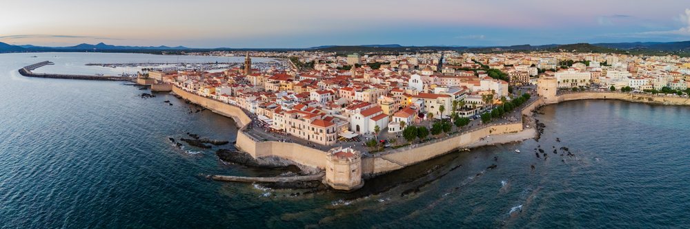 Aerial panoramic view of Alghero Old City at dusk showing ancient walls, harbor, and Mediterranean coastline, Travel Images, Sardinia, Italy.