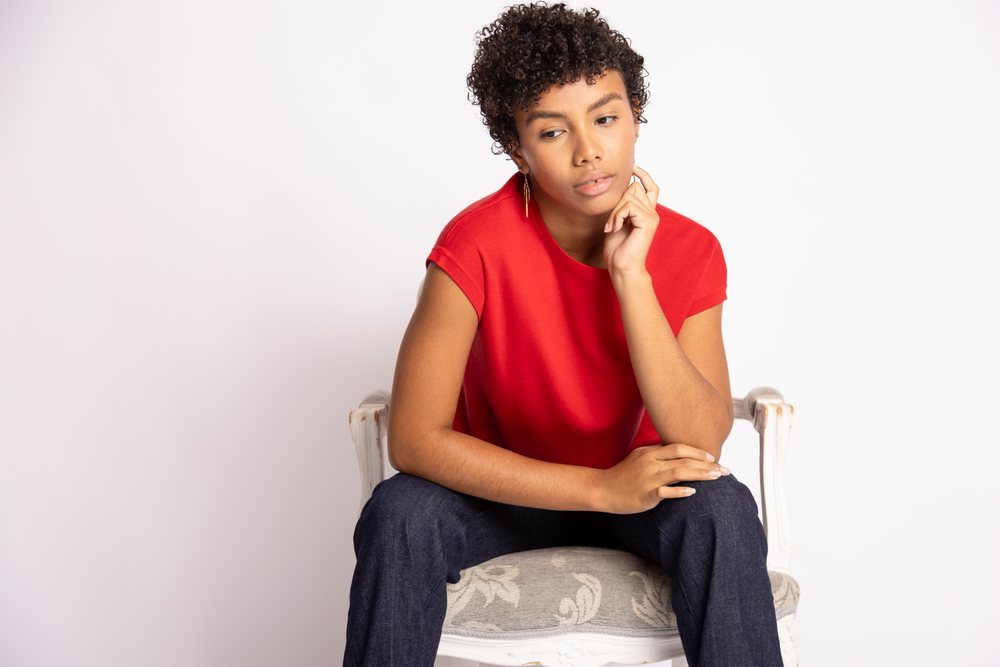Woman sitting thoughtfully on a white upholstered chair in a studio with a white background, fashion, clothes, young culture.