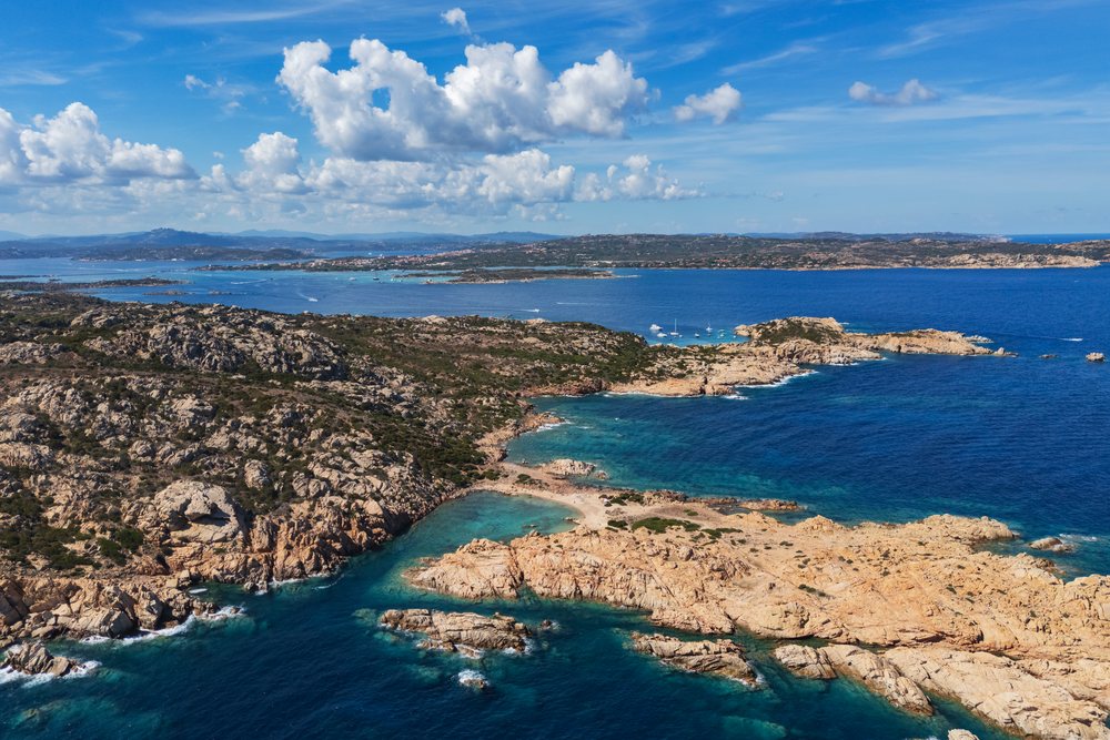 Rocky coastline of Spiagga di Punta Crucitta with turquoise Mediterranean Sea and boats near islands under a blue sky, Travel Images, La Maddalena, Sardinia, Italy.