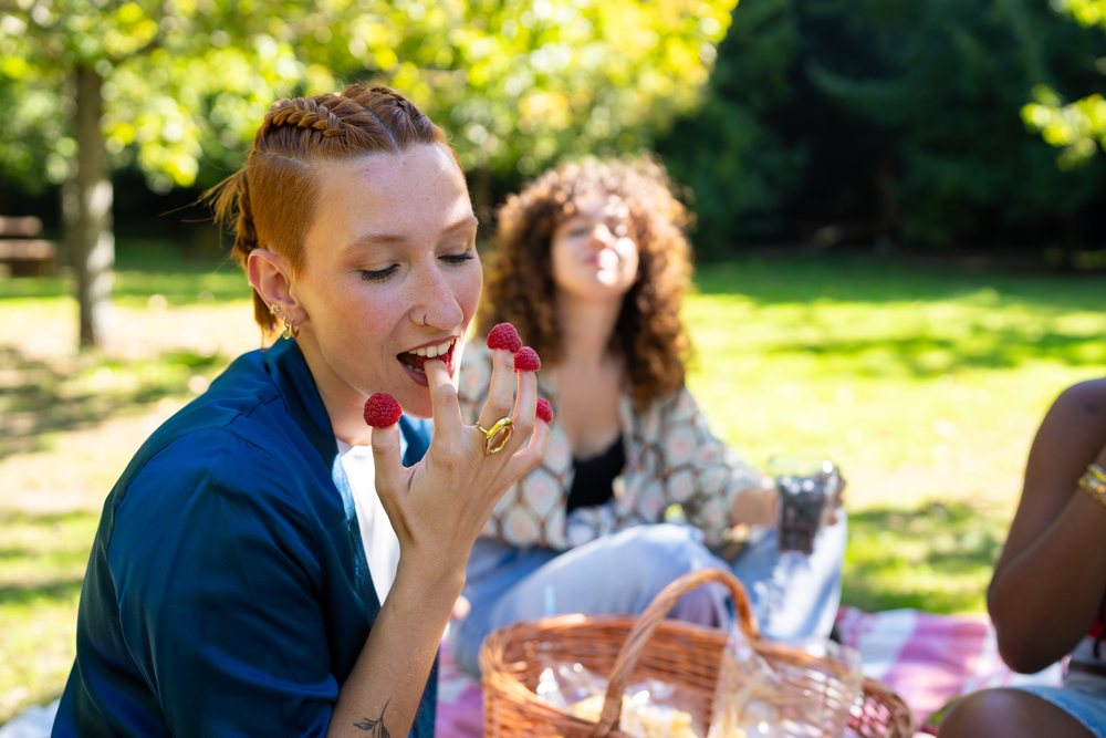 Woman with braided hair enjoys fresh raspberries on her fingers during a picnic on a blanket in a sunlit park, Spain.