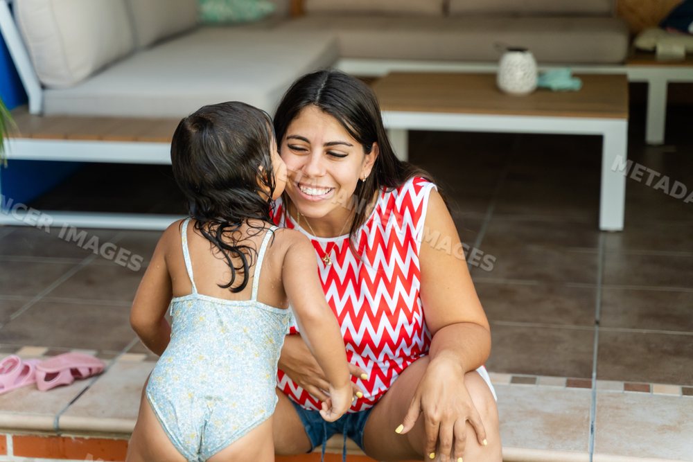 A white child kisses a smiling woman sitting on a patio in Madrid