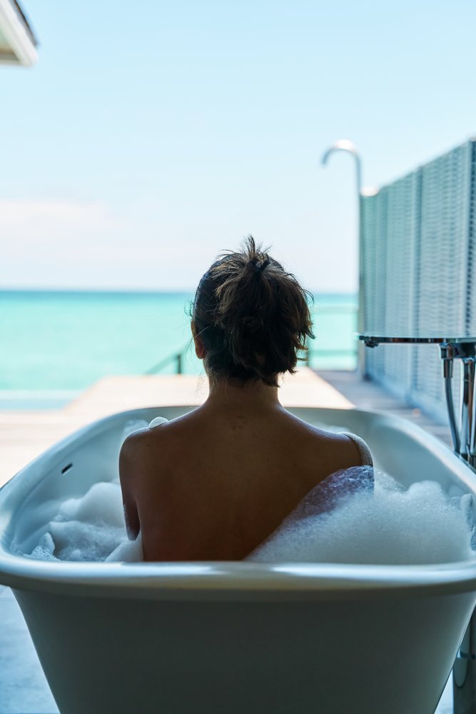 A woman relaxing in a bubble bath with a scenic ocean view in the, Maldives.