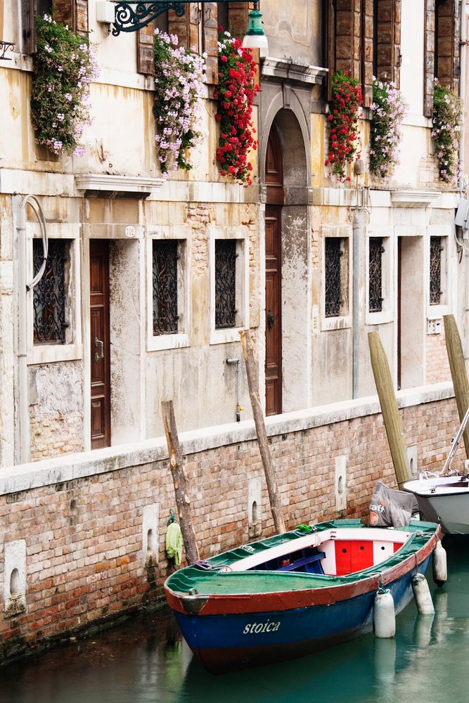 Rowboats moored on a canal beside a historic building with flower baskets, Venice, Veneto, Italy.