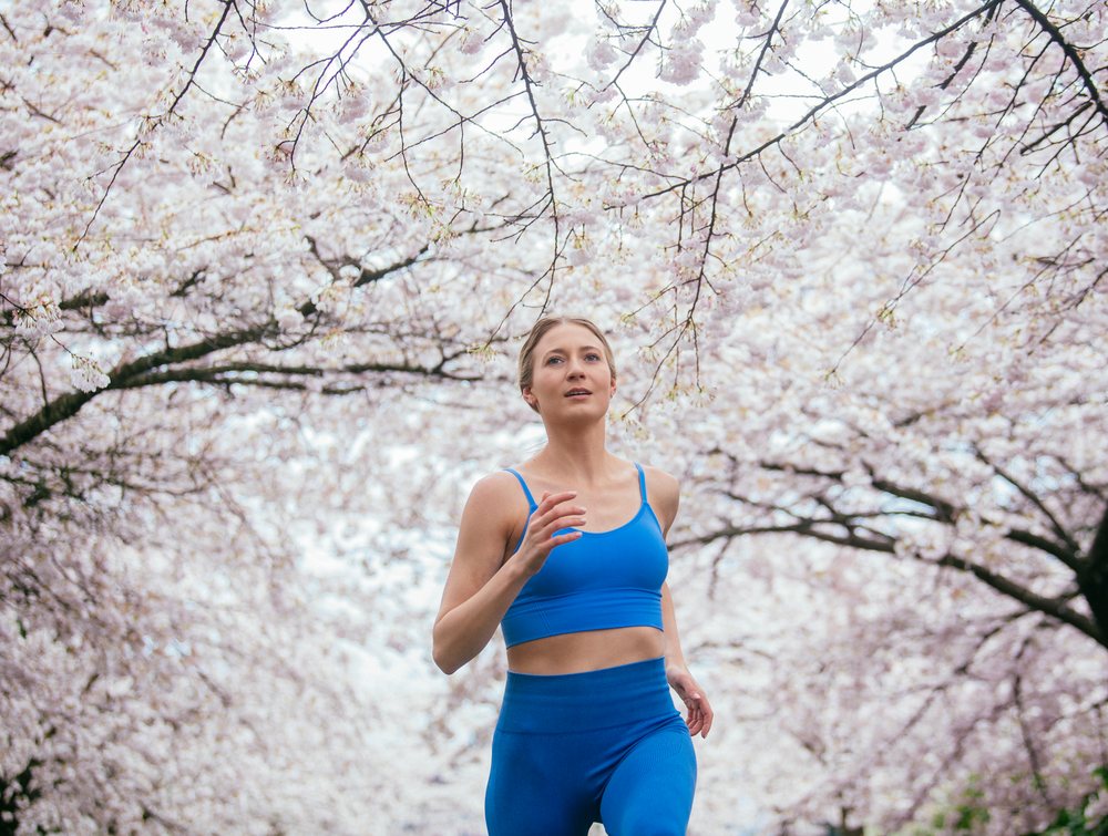 Woman running outdoors during spring, surrounded by blooming cherry blossoms, USA.