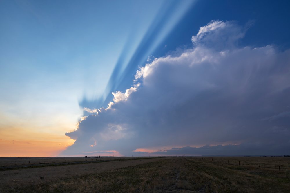 Crepuscular rays shine through a storm cloud over open fields at Sunset, Storm Chasing, Weather, Environment, Grover, Colorado, USA.