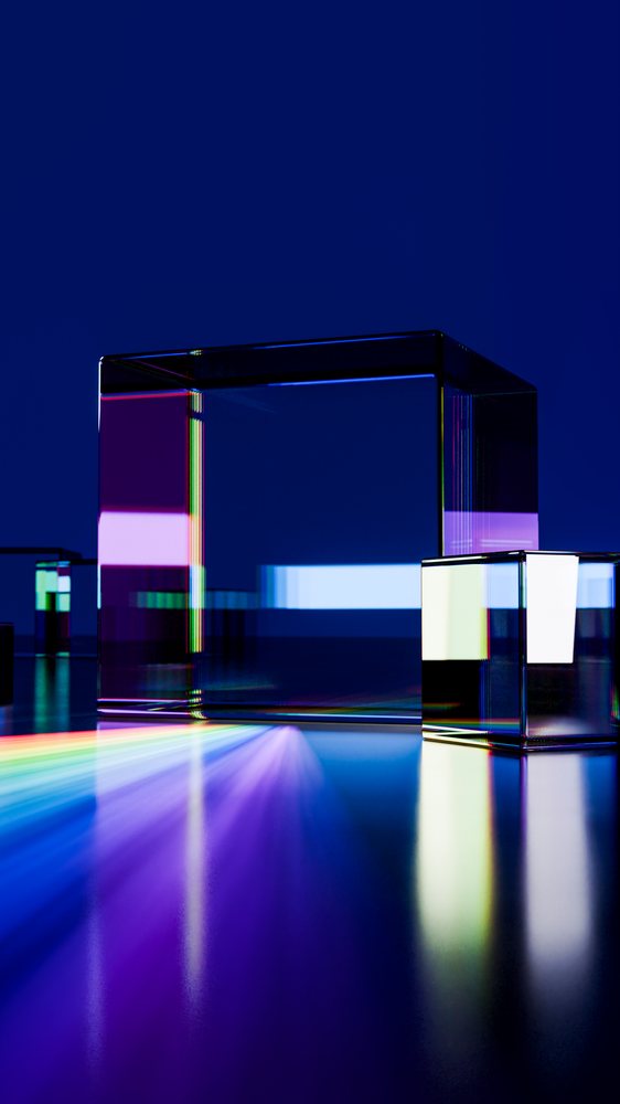 Transparent glass cubes on a reflective surface refract a rainbow of prism light against a dark blue background in a studio setting.