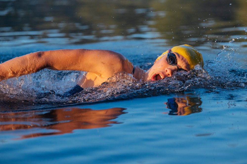 Person wearing a yellow swimming cap and goggles performing freestyle stroke in open water, USA.