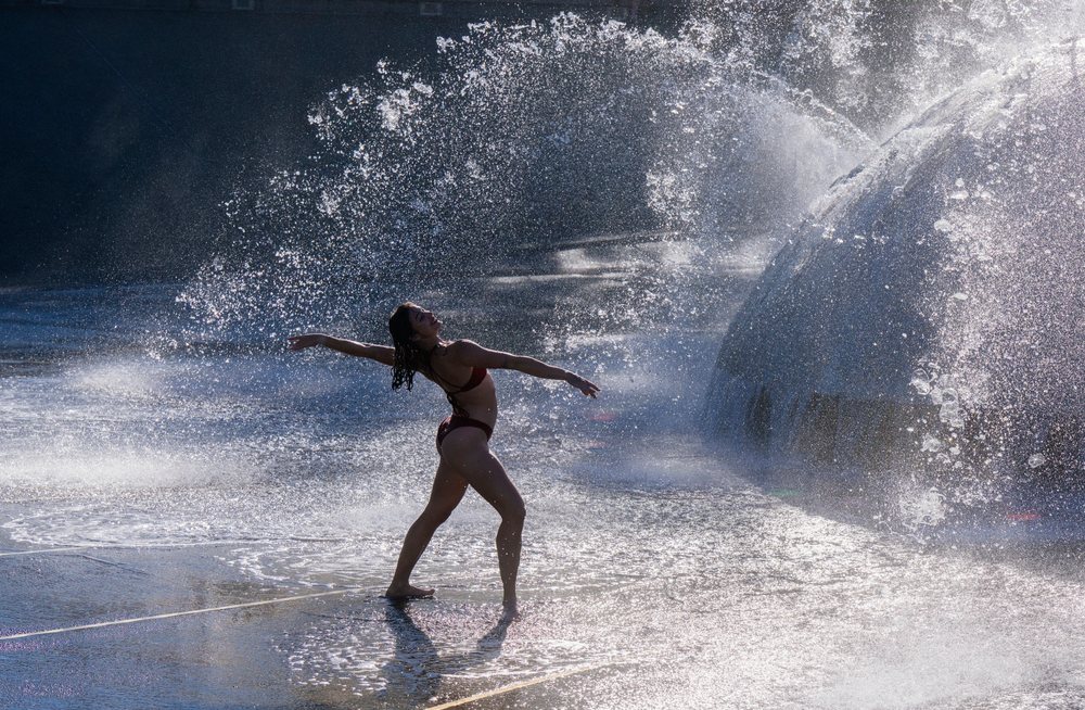 Woman dancing playfully and enjoying splashing water from an outdoor fountain in the USA on a sunny day, partner, acrobatics, yoga.