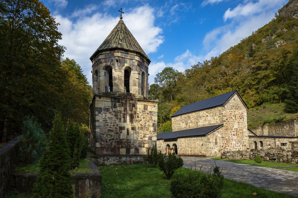 Green Monastery stone church and tower in wooded mountainous landscape, Georgia under blue sky with clouds, Chitakhevi.