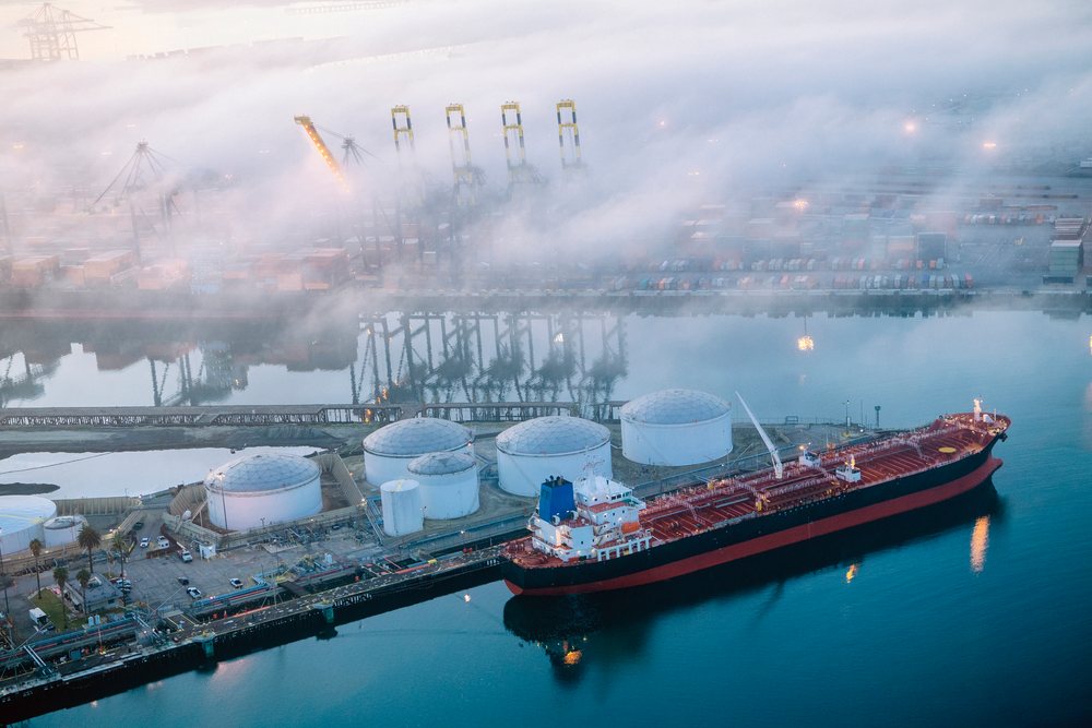 Cargo ship docked at a container terminal near oil storage tanks under morning mist at the, Port of Long Beach, CA, USA.
