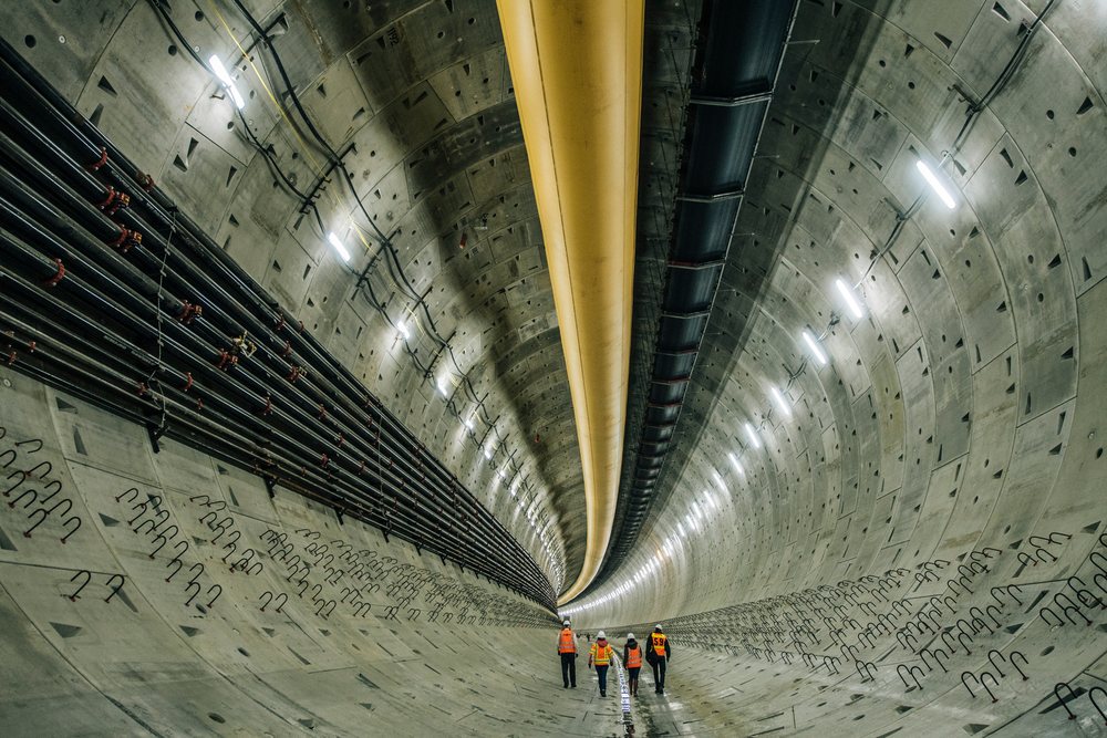Four construction workers wearing safety vests and hard hats walk inside a large concrete tunnel under construction, Bertha, drilling, USA.