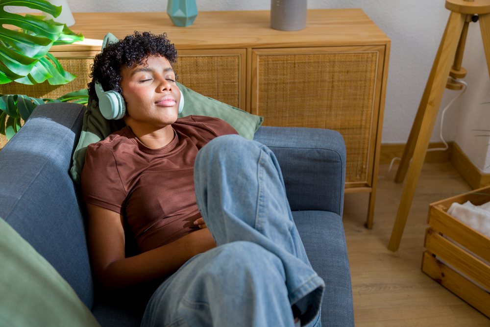 Woman wearing headphones relaxes on a blue sofa in her living room, Young woman, home.