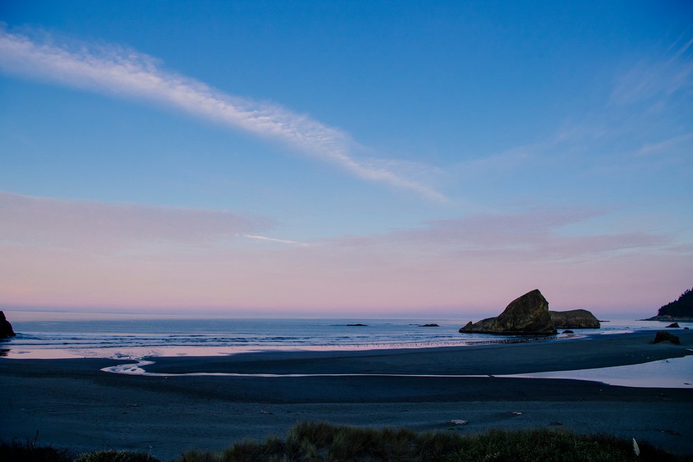 Rock formations on a sandy beach by the ocean with clouds in the sky at sunset near Meyers Creek, Oregon, USA.