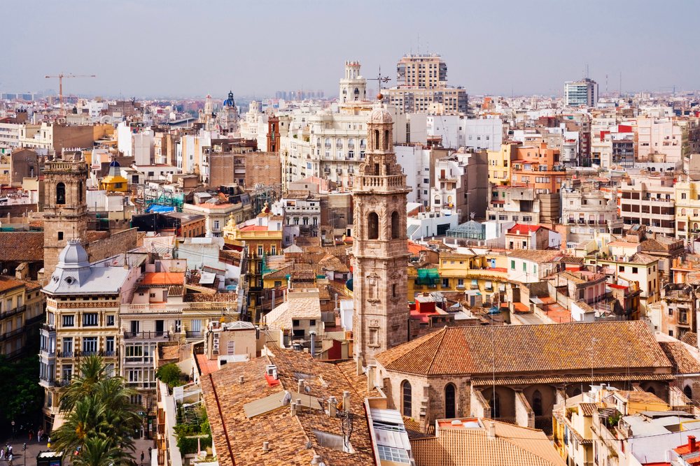 Valencia city skyline featuring a historic church tower, urban rooftops, and high-rise buildings under a clear daylight sky.