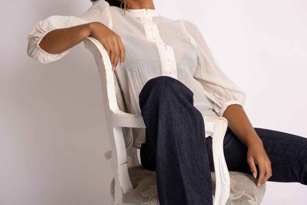 Woman in white buttoned blouse and blue jeans sitting on a white vintage chair in a minimalist setting, fashion, young culture.