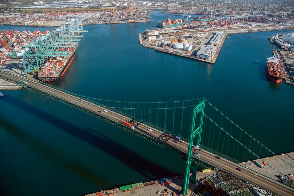 Suspension bridge crossing water at an industrial port with container ships, cranes, and cargo terminals in view, industrial port, CA, USA.