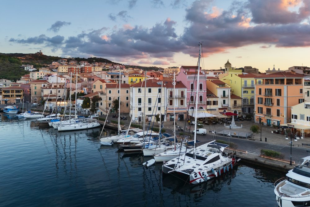 Boats and yachts docked in a harbour at Dawn, with colorful Mediterranean buildings along the waterfront, Travel Images, La Maddalena, Sardinia, Italy.