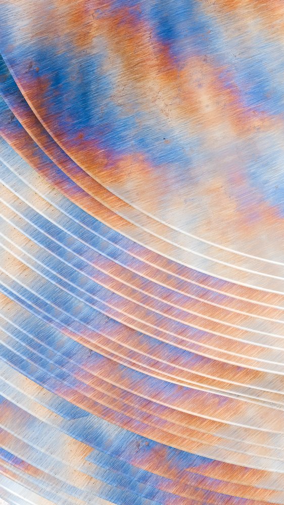 Rusted metal surface with curved lines and colorful oxidation patterns blending blue and orange hues.
