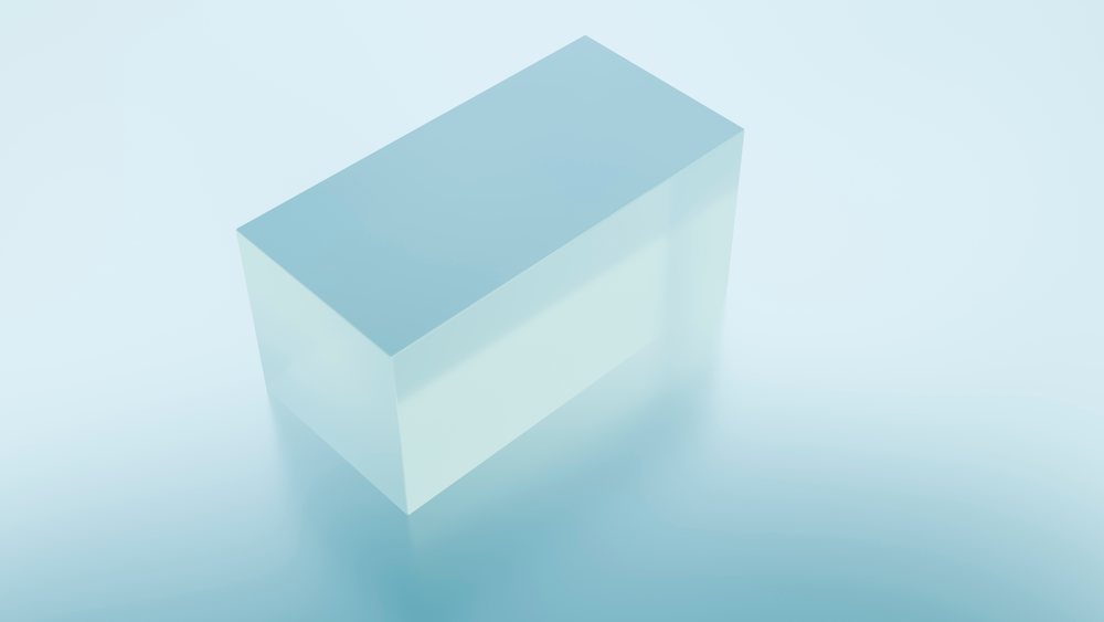 Transparent rectangular prism with a blue tint softly reflects on a smooth surface in a minimalist studio setting.