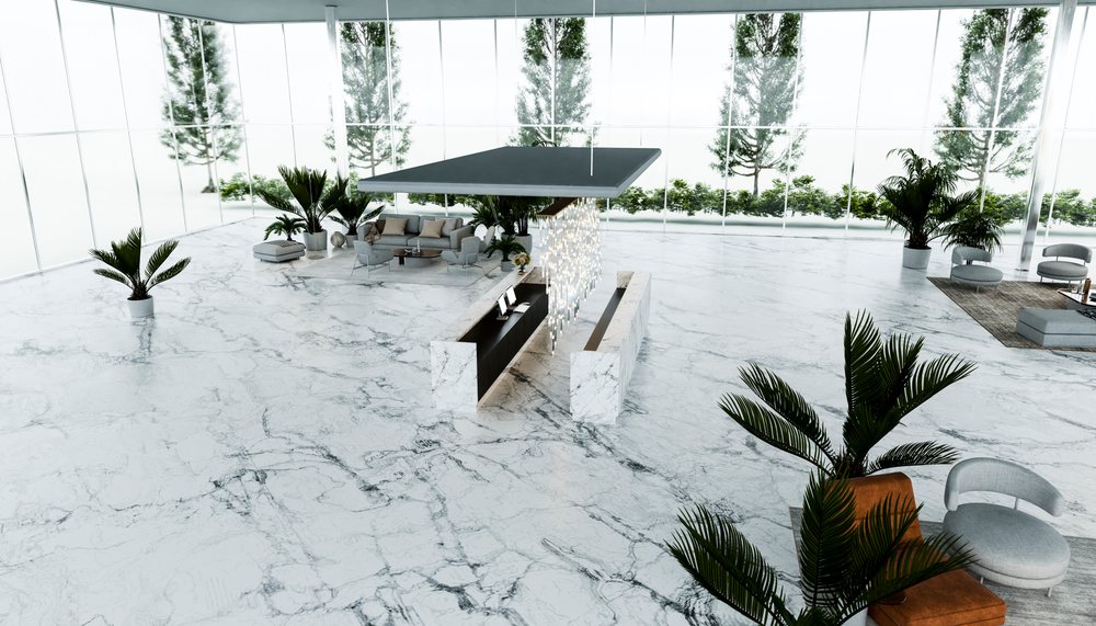Modern lobby interior with marble floors, glass walls, reception desk, and seating area with plants under natural light.