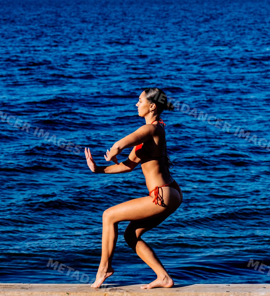 Woman in red swimsuit doing squat exercise by the water in washington
