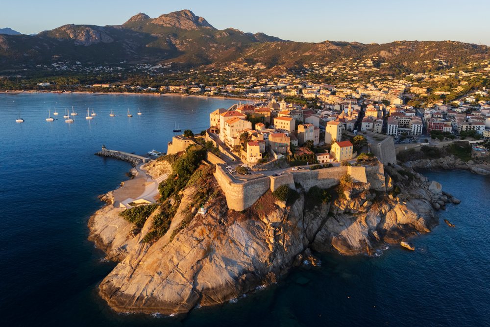 The Citadel of Calvi perched on a rocky cliff overlooks the sea with boats nearby at Sunrise, Travel Photography, Corsica, France.