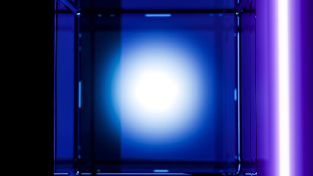 Transparent glass cube illuminated by blue glowing light and neon reflections against a dark background.
