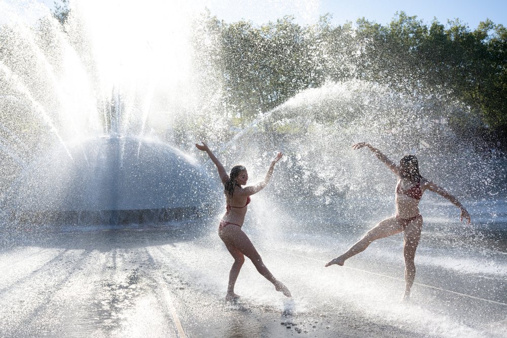 Women in swimwear dancing and playing in a water fountain on a sunny day, partner, acrobatics, yoga, USA.