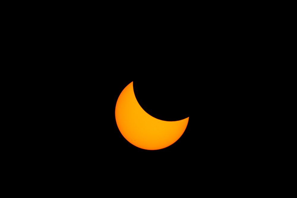 Partial solar eclipse showing the moon covering part of the sun with visible sunspots, USA under a black sky, Los Angeles.