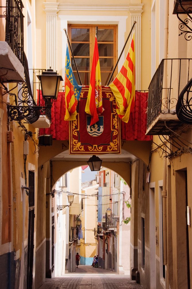 Archway with flags and lamps over a cobblestone pedestrian street with balconies Joiosa, La Vila.
