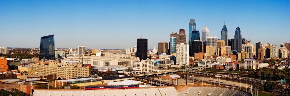 Philadelphia city skyline with high-rise buildings, a stadium, roads, and a bridge under a clear blue daytime sky, Pennsylvania, USA.